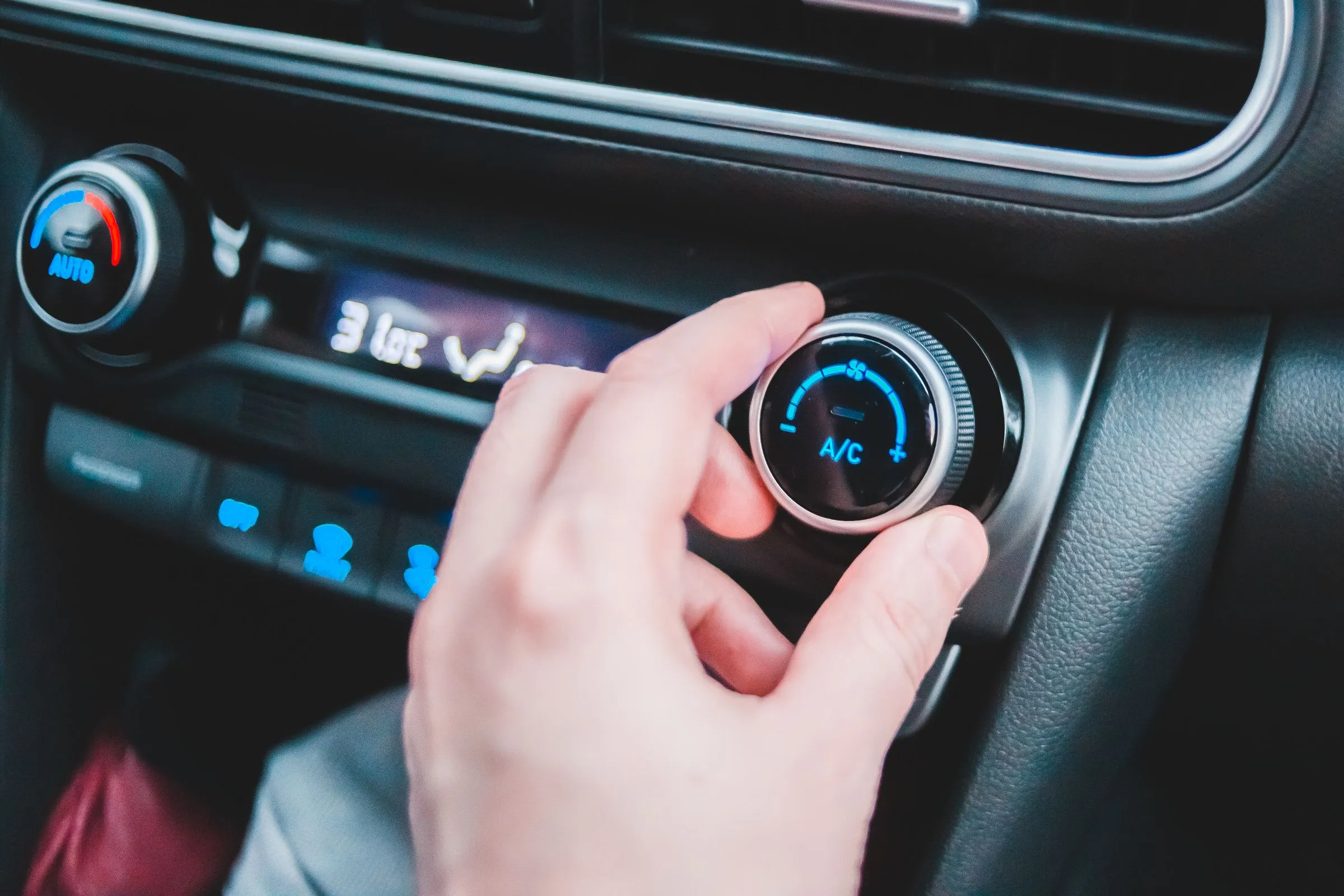 A driver’s hand turning the A/C dial on a car’s climate control panel.
