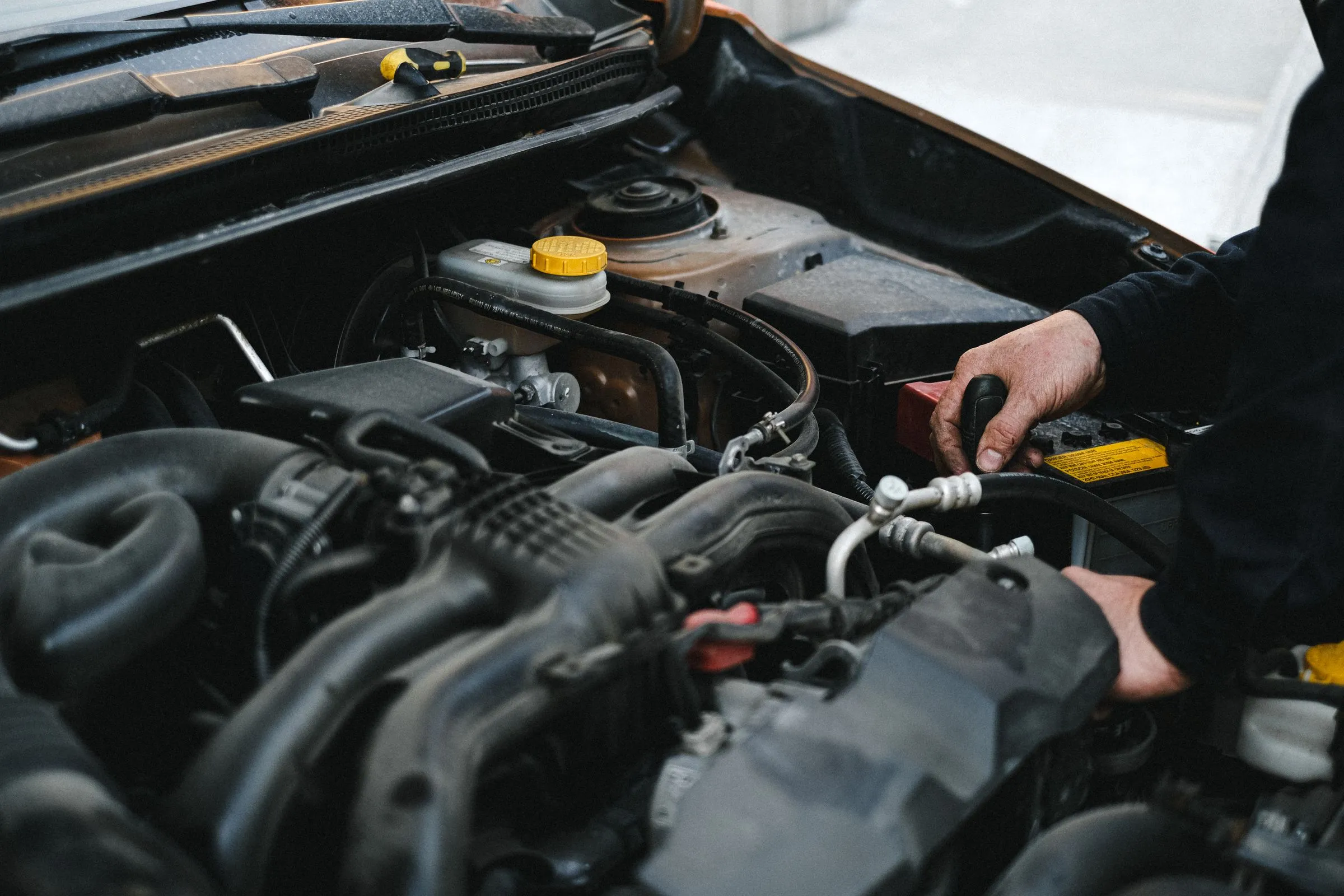 A technician’s hands working in the engine bay of a car.